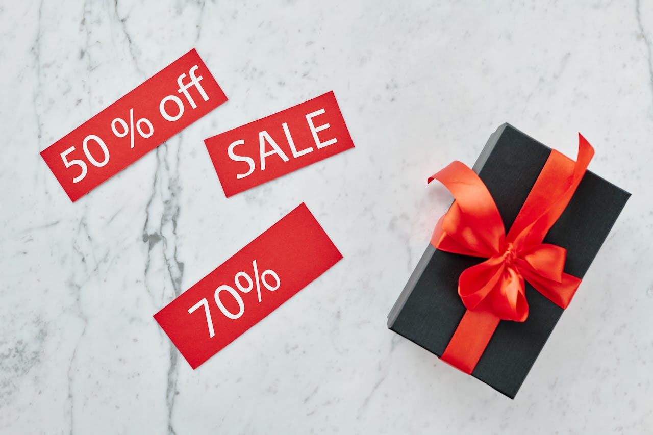 Stylish black gift box with red ribbon and sale tags on marble, perfect for Black Friday promotions.