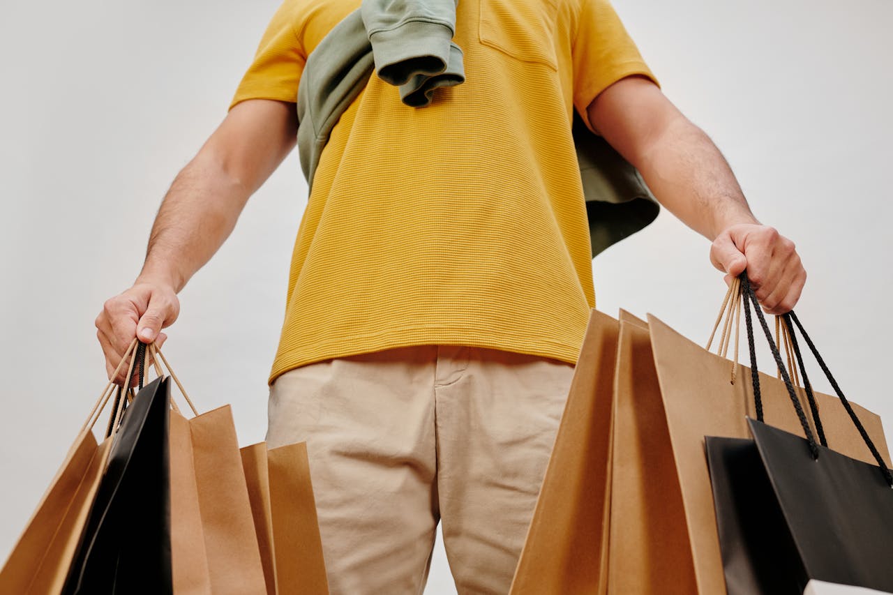 A young adult carrying paper shopping bags symbolizes retail therapy and consumerism indoors.